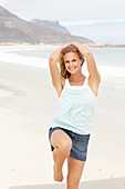 Junge blonde Frau im hellblauen Shirt und Jeansrock am Strand