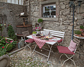 Gedeckter Tisch mit Stühlen und Bank neben Vintage Weinpresse auf Steinterrasse