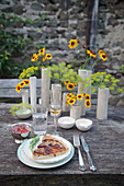 Piece of quiche and ceramic vases of flowers on garden table