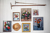 Floral pictures, vintage rakes and hat on white-painted wooden wall