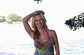 A young blonde woman on a beach wearing a purple bikini top and a summer dress