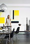 Frau deckt den Tisch im modernen Esszimmer mit gelben Bildern