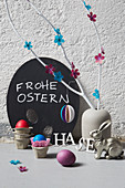 Vase of branches decorated with paper flowers, Easter bunny and Easter eggs in egg box cells