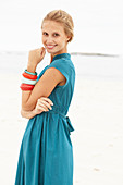 A young blonde woman on a beach wearing a blue summer dress