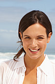 A young brunette woman on a beach wearing a white summer dress
