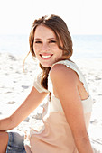 A young brunette woman on a beach wearing a beige top