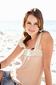 A young brunette woman on a beach wearing a beige top