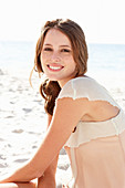 A young brunette woman on a beach wearing a beige top