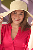 A young brunette woman wearing a dark pink blouse and a summer hat