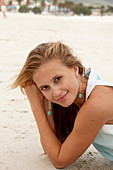 A young blonde woman on a beach wearing a light-blue top