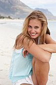 A young blonde woman on a beach wearing a light-blue top