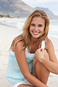 A young blonde woman on a beach wearing a light-blue top