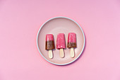 Colorful pink and brown popsicles lying in row on pastel plate