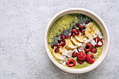 Bowl with green smoothie garnished with various seeds and berries with banana