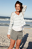 A brunette woman on a sandy beach wearing a striped top and shorts