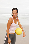 Junge brünette Frau mit Ball in sportlicher Kleidung am Meer
