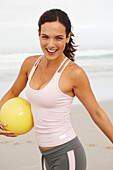 A young brunette woman by the sea wearing sports clothes with a ball
