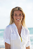 A young blonde woman on a beach wearing a white blouse