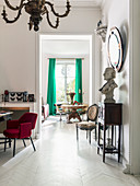 Bust on console table below mirror on wall and red upholstered chair in anteroom