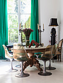 Runder Holztisch mit geschnitztem Tischbein und Klassikerstühle vor Fenster mit grünem Vorhang