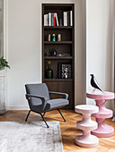 Moderne rosafarbene Beistelltische und ein Sessel vorm Regal