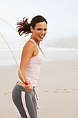 A young brunette woman on a beach wearing a sports outfit with a skipping rope