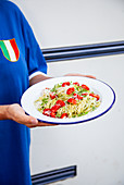 A woman serving a plate of spaghetti with pesto and cherry tomatoes
