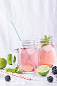 Two drinking jars with refreshing lemonade containing lime and blackberry