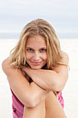 A young blonde woman on a beach wearing a pink top and a bikini