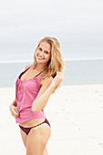 Junge blonde Frau im rosa Top und Bikini am Strand