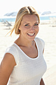 Reife blonde Frau im weißen Top am Strand