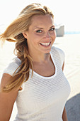 A mature blonde woman on a beach wearing a white top