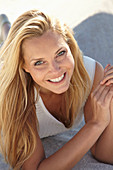 A mature blonde woman lying on a sandy beach wearing a white top