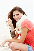 A brunette woman on a beach wearing a scarf and a salmon-coloured top