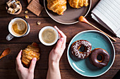 Hand hält Kaffeebecher, Croissant und Donuts