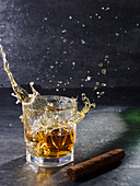 Crystal glass with splashing whiskey drink and thick cigar