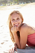 A young blonde woman on a beach wearing a pink top