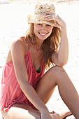 A young blonde woman on a beach wearing a pink top and a beige hat