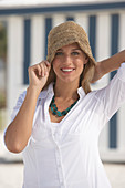 A young blonde woman on a beach wearing a white blouse and a brown hat