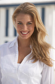 A young blonde woman on a beach wearing a white blouse