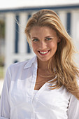 A young blonde woman on a beach wearing a white blouse