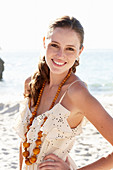 A young brunette woman on a beach wearing a light summer dress and a necklace
