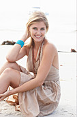 A blonde woman on a beach wearing a beige summer dress