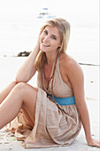 A blonde woman on a beach wearing a beige summer dress