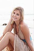 A blonde woman on a beach wearing a beige summer dress