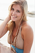 A blonde woman on a beach wearing a beige summer dress