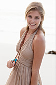 A blonde woman on a beach wearing a beige summer dress