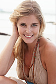 A blonde woman on a beach wearing a beige summer dress