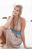 A blonde woman on a beach wearing a beige summer dress