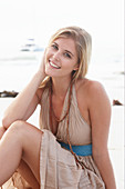 A blonde woman on a beach wearing a beige summer dress